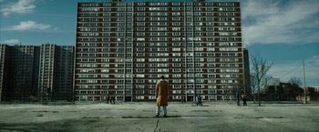 Movie still from “Candyman” (2021), directed by Nia DaCosta – A person standing in front of a tall building; Extreme Wide shot, Low angle