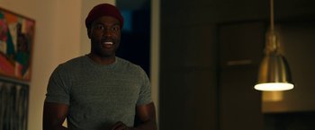 Movie still from “Candyman” (2021), directed by Nia DaCosta – A man wearing a red hat smiling for the camera; Medium shot, Over the shoulder angle