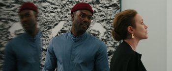 Movie still from “Candyman” (2021), directed by Nia DaCosta – A man wearing a red hat talking to a woman; Medium shot, Over the shoulder angle