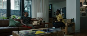 Movie still from “Candyman” (2021), directed by Nia DaCosta – Two men are sitting in a living room talking to each other; Wide shot, Over the shoulder angle