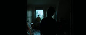 Movie still from “Candyman” (2021), directed by Nia DaCosta – A woman standing in a room with a painting in the background; Medium shot, Over the shoulder angle