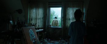 Movie still from “Candyman” (2021), directed by Nia DaCosta – A man looking out of a window in a room; Wide shot, Low angle