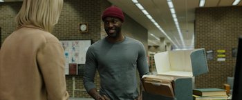 Movie still from “Candyman” (2021), directed by Nia DaCosta – A man with a red hat standing in front of a book case; Medium shot, Low angle