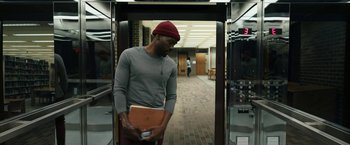 Movie still from “Candyman” (2021), directed by Nia DaCosta – A young man holding a laptop in a hallway; Medium shot, Low angle