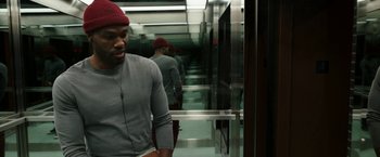 Movie still from “Candyman” (2021), directed by Nia DaCosta – A man with a red hat standing in an elevator; Medium shot, Overhead angle