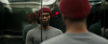 Movie still from “Candyman” (2021), directed by Nia DaCosta – A man in a red hat looking into a mirror; Close Up shot, Over the shoulder angle