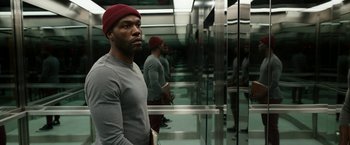 Movie still from “Candyman” (2021), directed by Nia DaCosta – A man standing in an elevator with his head turned to the side; Medium shot, Overhead angle