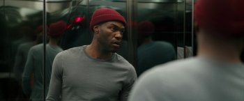 Movie still from “Candyman” (2021), directed by Nia DaCosta – A man with a red hat is sitting on a train; Close Up shot, Over the shoulder angle