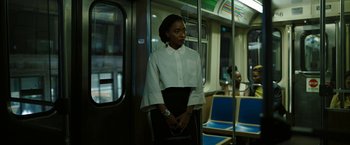Movie still from “Candyman” (2021), directed by Nia DaCosta – A woman standing on a train holding her purse; Medium shot, Over the shoulder angle