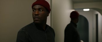 Movie still from “Candyman” (2021), directed by Nia DaCosta – A man wearing a red hat looking into a mirror; Close Up shot, Over the shoulder angle