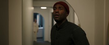 Movie still from “Candyman” (2021), directed by Nia DaCosta – A man in a black shirt wearing a red hat; Close Up shot, Over the shoulder angle