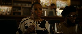 Movie still from “Candyman” (2021), directed by Nia DaCosta – A woman sitting at a table holding a necklace in her hand; Close Up shot, Over the shoulder angle