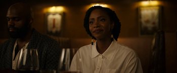 Movie still from “Candyman” (2021), directed by Nia DaCosta – A woman sitting at a table in front of a glass of wine; Close Up shot, Over the shoulder angle