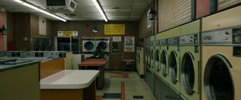 Movie still from “Candyman” (2021), directed by Nia DaCosta – A person sitting at a table in a room with many machines; Extreme Wide shot, High angle