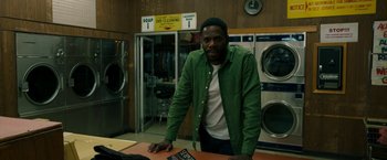 Movie still from “Candyman” (2021), directed by Nia DaCosta – A man standing in front of a counter in a laundromat; Medium shot, Over the shoulder angle