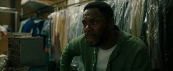 Movie still from “Candyman” (2021), directed by Nia DaCosta – A man in a green shirt is in front of a rack of clothes; Close Up shot, Low angle