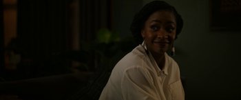 Movie still from “Candyman” (2021), directed by Nia DaCosta – A woman in a white shirt is smiling for the camera; Close Up shot, Over the shoulder angle