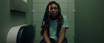 Movie still from “Candyman” (2021), directed by Nia DaCosta – A person with dreadlocks sitting in a room; Medium shot, Overhead angle