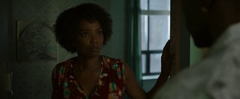 Movie still from “Candyman” (2021), directed by Nia DaCosta – A woman in a red and white floral shirt is looking at the camera; Close Up shot, Over the shoulder angle