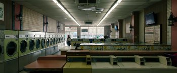 Movie still from “Candyman” (2021), directed by Nia DaCosta – A woman standing in front of machines in a laundromat; Extreme Wide shot, Low angle