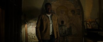Movie still from “Candyman” (2021), directed by Nia DaCosta – A man standing in front of a wall covered in graffiti; Medium shot, Over the shoulder angle