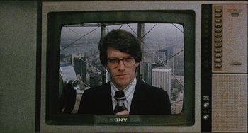 Movie still from “Cannibal Holocaust” (1980), directed by Ruggero Deodato – A man wearing a suit and tie standing in front of a tv; Close Up shot, Low angle