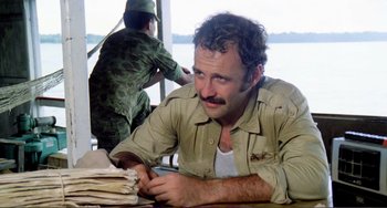 Movie still from “Cannibal Holocaust” (1980), directed by Ruggero Deodato – A man sitting at a table with a man standing next to him; Close Up shot, Low angle