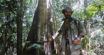 Movie still from “Cannibal Holocaust” (1980), directed by Ruggero Deodato – A man standing next to a tree in the woods; Medium shot, Low angle