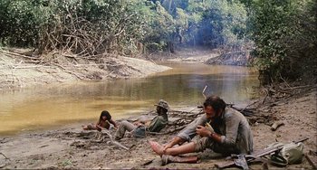 Movie still from “Cannibal Holocaust” (1980), directed by Ruggero Deodato – A group of people sitting on the ground near a body of water; Wide shot, High angle
