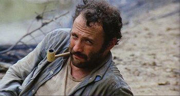Movie still from “Cannibal Holocaust” (1980), directed by Ruggero Deodato – A man with curly hair is holding a pipe in his mouth; Close Up shot, High angle