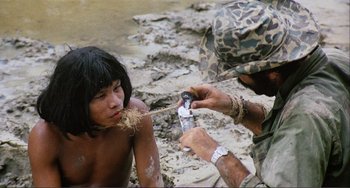 Movie still from “Cannibal Holocaust” (1980), directed by Ruggero Deodato – A man in a camouflage hat is shaving a boy's face; Medium shot, High angle