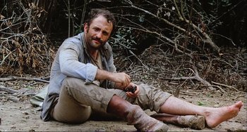 Movie still from “Cannibal Holocaust” (1980), directed by Ruggero Deodato – A man sitting on the ground holding a knife; Medium shot, Low angle