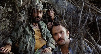 Movie still from “Cannibal Holocaust” (1980), directed by Ruggero Deodato – A group of men sitting next to each other in the woods; Medium shot, Low angle