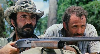 Movie still from “Cannibal Holocaust” (1980), directed by Ruggero Deodato – Two men with guns in a forest; Medium shot, Low angle