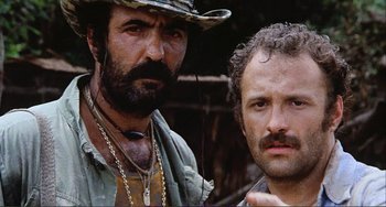 Movie still from “Cannibal Holocaust” (1980), directed by Ruggero Deodato – Two men standing next to each other in the woods; Close Up shot, Low angle