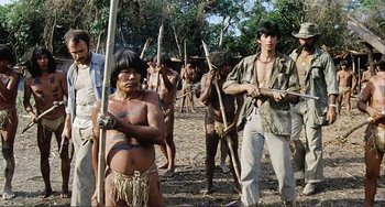 Movie still from “Cannibal Holocaust” (1980), directed by Ruggero Deodato – A group of people standing in the woods holding wooden sticks; Medium shot, Low angle