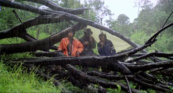 Movie still from “Cannibal Holocaust” (1980), directed by Ruggero Deodato – A group of men sitting on top of a pile of tree branches; Wide shot, Low angle