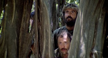 Movie still from “Cannibal Holocaust” (1980), directed by Ruggero Deodato – A couple of men standing next to each other in the woods; Medium shot, Low angle