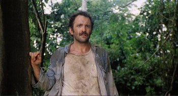 Movie still from “Cannibal Holocaust” (1980), directed by Ruggero Deodato – A man with a beard is standing in the woods; Medium shot, Low angle