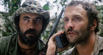 Movie still from “Cannibal Holocaust” (1980), directed by Ruggero Deodato – Two men in the woods are talking on a walkie - talkie; Close Up shot, Low angle