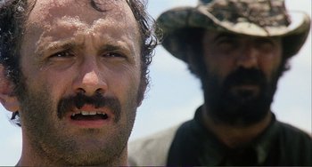 Movie still from “Cannibal Holocaust” (1980), directed by Ruggero Deodato – A man with a mustache and a beard and another man with a beard and a hat; Close Up shot, Low angle