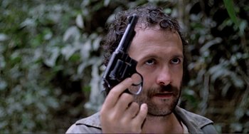 Movie still from “Cannibal Holocaust” (1980), directed by Ruggero Deodato – A man holding a gun up to his face; Close Up shot, Low angle
