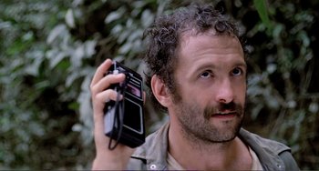 Movie still from “Cannibal Holocaust” (1980), directed by Ruggero Deodato – A man with a beard holding up a radio in his hand; Close Up shot, Low angle