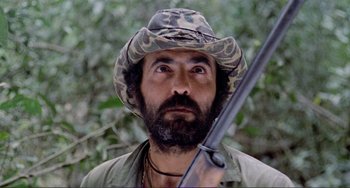 Movie still from “Cannibal Holocaust” (1980), directed by Ruggero Deodato – A man with a beard holding a rifle in his hand; Close Up shot, Low angle