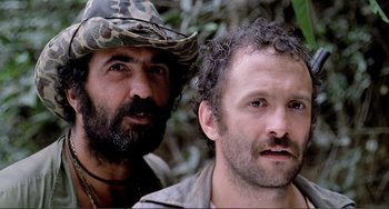 Movie still from “Cannibal Holocaust” (1980), directed by Ruggero Deodato – Two men standing next to each other in the woods; Close Up shot, Low angle