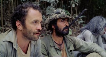 Movie still from “Cannibal Holocaust” (1980), directed by Ruggero Deodato – A couple of men sitting next to each other in the woods; Close Up shot, Low angle