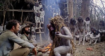 Movie still from “Cannibal Holocaust” (1980), directed by Ruggero Deodato – A group of people sitting around a fire in the woods; Wide shot, High angle