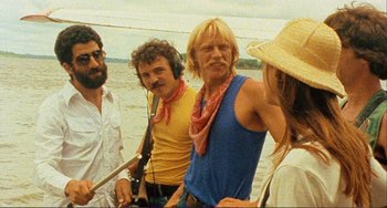 Movie still from “Cannibal Holocaust” (1980), directed by Ruggero Deodato – A group of men standing next to each other on a beach; Medium shot, Over the shoulder angle