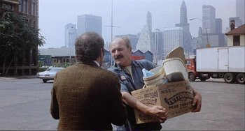 Movie still from “Cannibal Holocaust” (1980), directed by Ruggero Deodato – A man handing a box to another man on the street; Medium shot, Over the shoulder angle