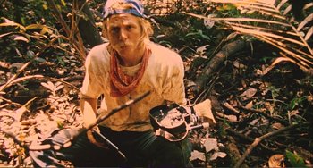 Movie still from “Cannibal Holocaust” (1980), directed by Ruggero Deodato – A man sitting on the ground holding a camera; Medium shot, Low angle